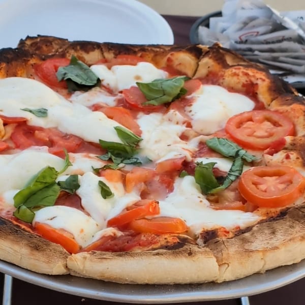 Wood-fired pizza with melted mozzarella, sliced tomatoes, and fresh basil.