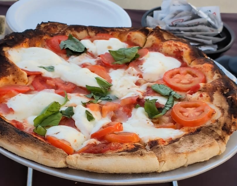 Wood-fired pizza with melted mozzarella, sliced tomatoes, and fresh basil.