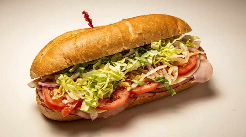 A large deli sub sandwich filled with ham, cheese, tomatoes, onions, and shredded lettuce.