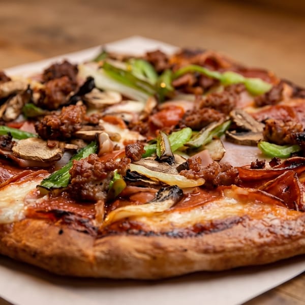 Delicious pizza with pepperoni, sausage, mushrooms, and green peppers on a wooden table.