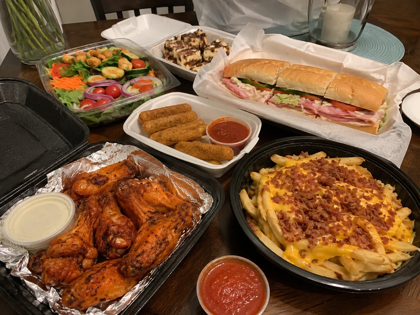 Family takeout meal with wings sandwiches salad and sides in Norco